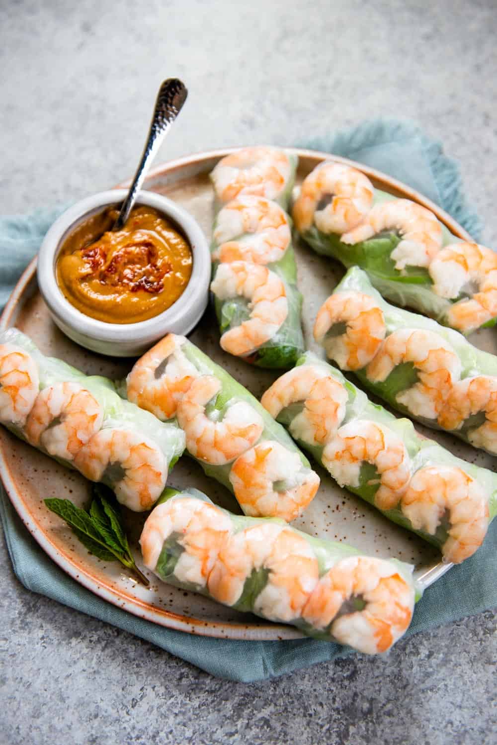 A plate of fresh shrimp spring rolls with visible shrimp and greens, served with a small bowl of peanut dipping sauce on a blue cloth napkin—perfect for those looking for healthy snacks or tasty after school snacks.