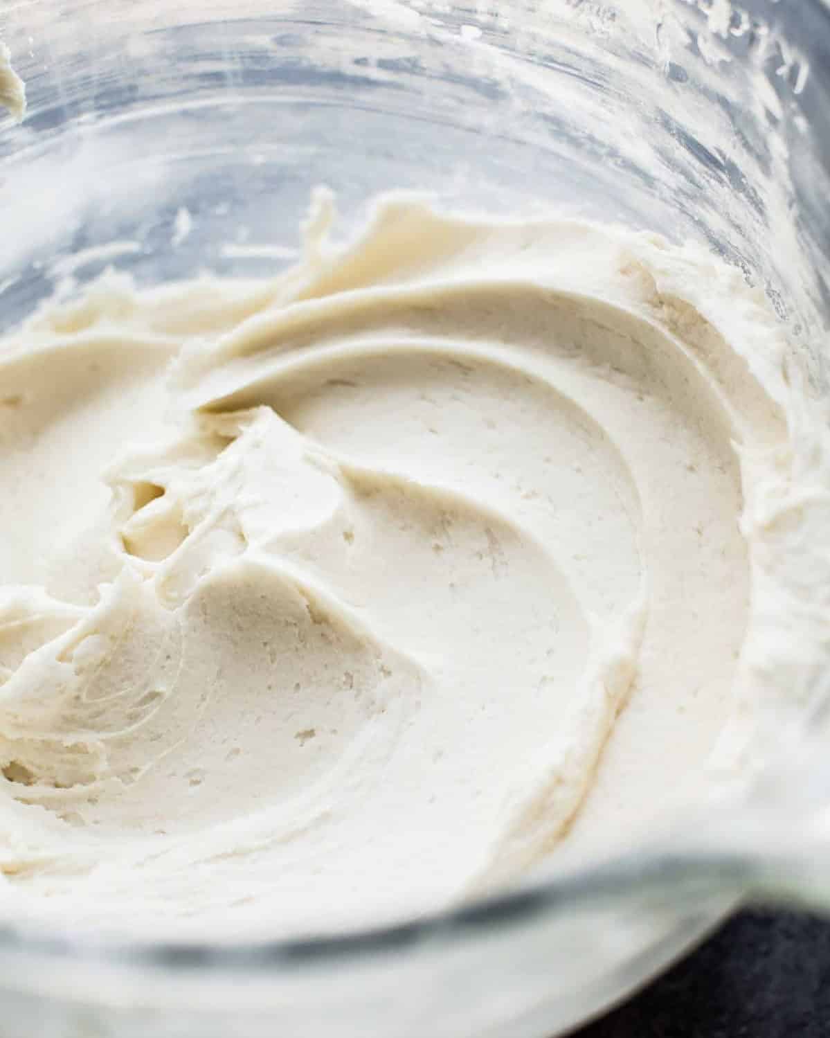 A close-up of creamy, smooth white frosting swirled in a glass mixing bowl.