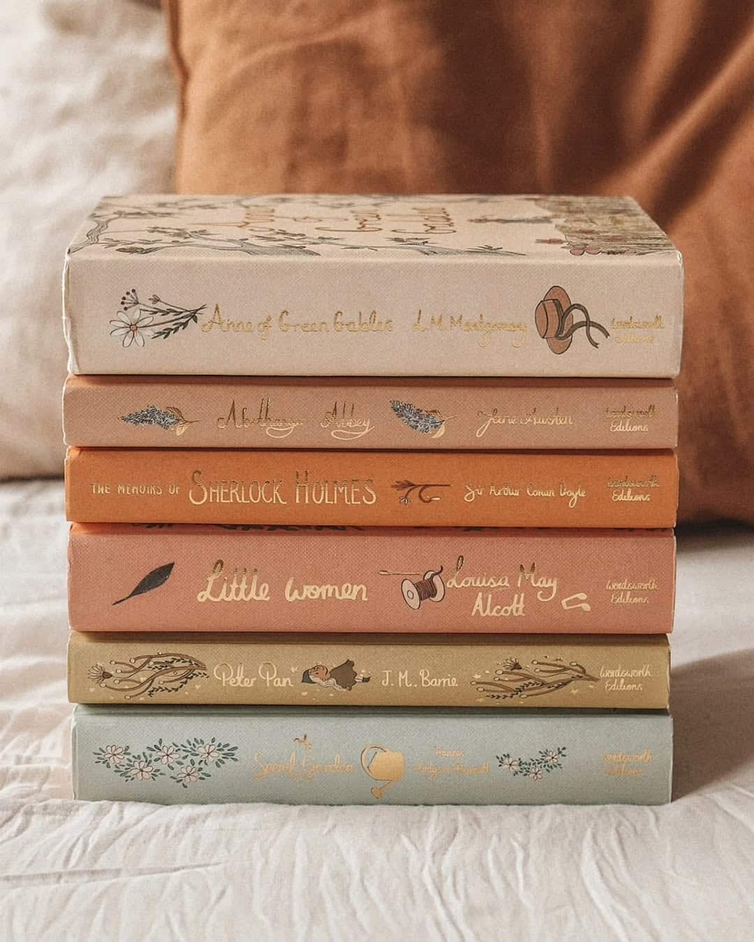 A stack of six vintage-style hardcover books with illustrated spines, including Anne of Green Gables, A Little Princess, Sherlock Holmes, Little Women, Peter Pan, and The Secret Garden.
