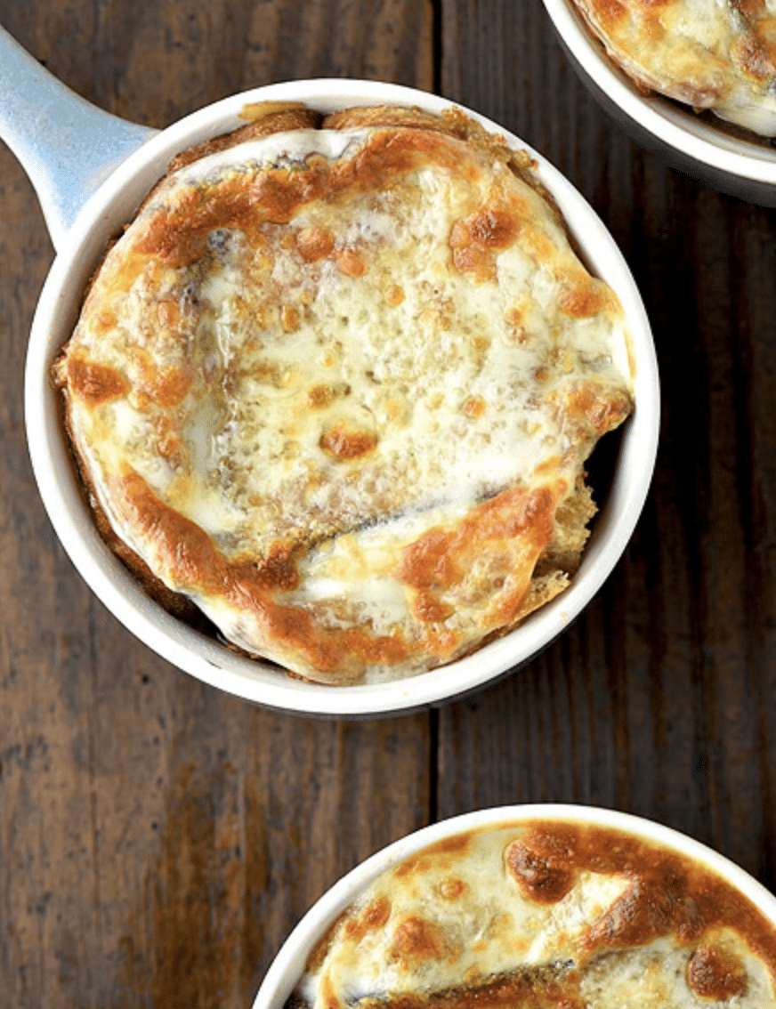 A bowl of French onion soup topped with a toasted bread slice and melted, golden-brown cheese, placed on a wooden surface.