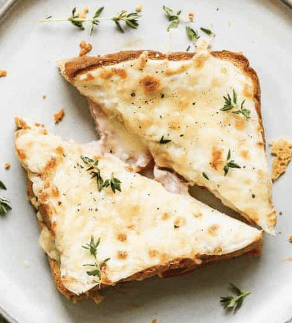 Two slices of toasted bread topped with melted cheese and herbs, cut into triangles, served on a white plate.
