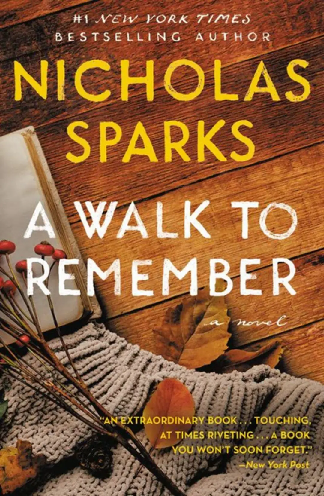 The cover of A Walk to Remember by Nicholas Sparks features an open notebook, brown leaves, and a knitted gray scarf on a wooden surface—an inviting addition to anyone’s TBR or books collection—with the title and author’s name in large yellow and white text.