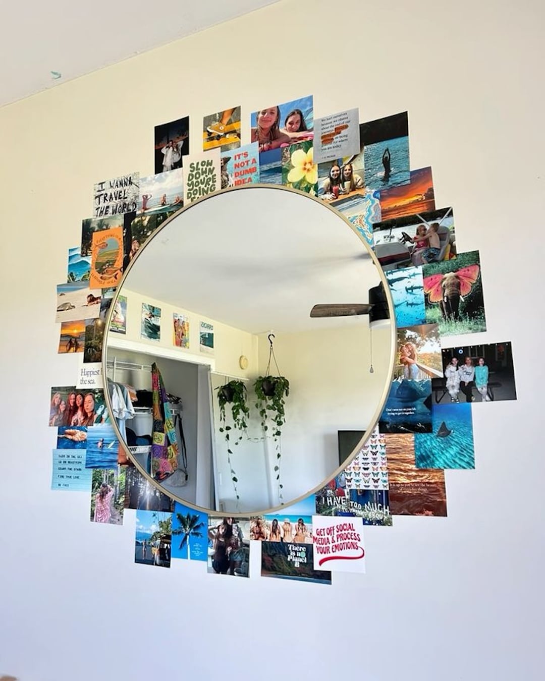 A round mirror is mounted on a wall, surrounded by colorful photos from summer activities with siblings and motivational quotes arranged in a circular collage. The mirror reflects a room with plants and part of a ceiling fan.