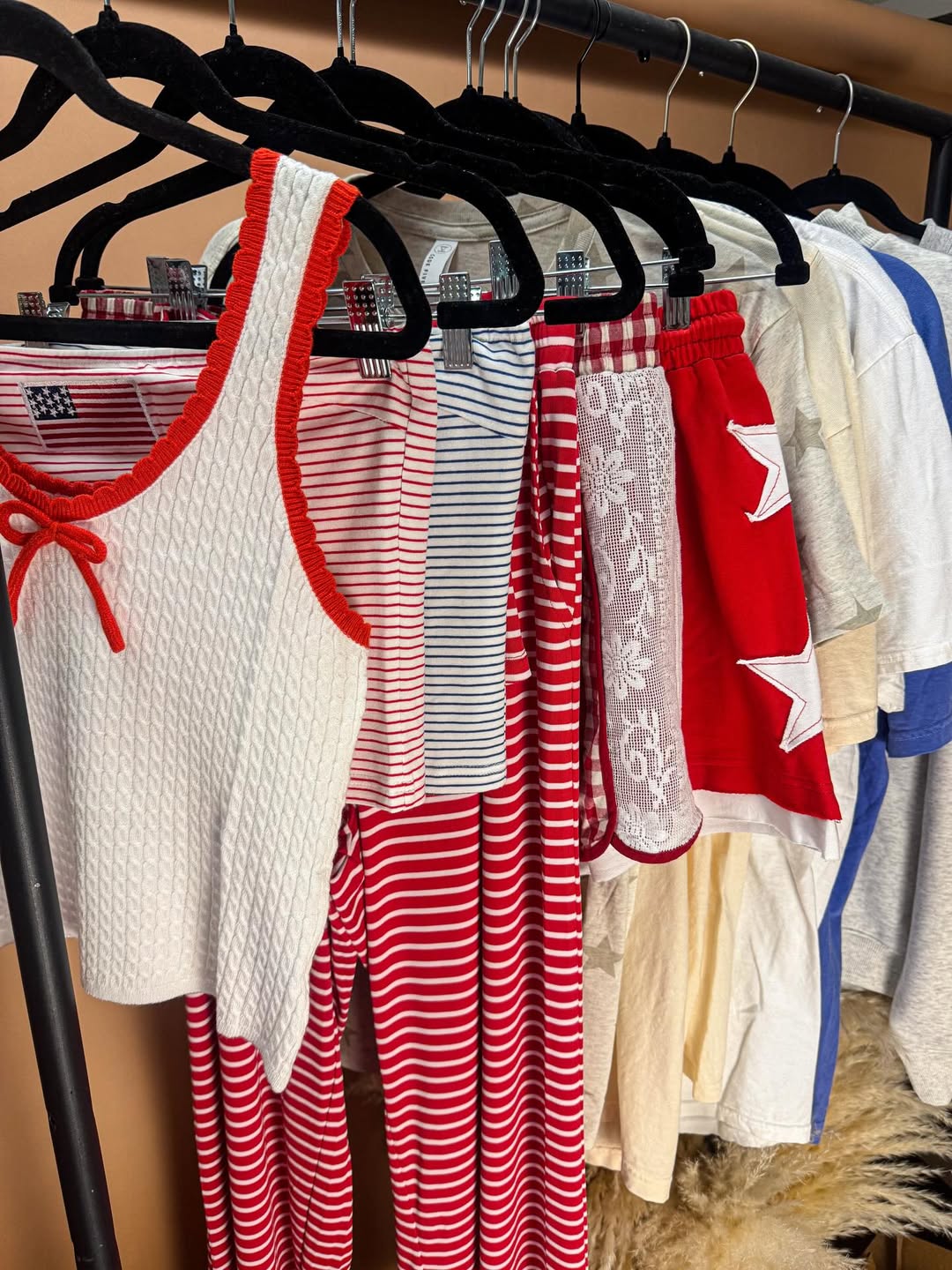 A clothing rack displays various summer outfits, including red and white striped shorts, a white tank top with red trim, and red shorts with white stars—perfect pieces for a stylish Fourth of July outfit or casual Independence Day fashion.
