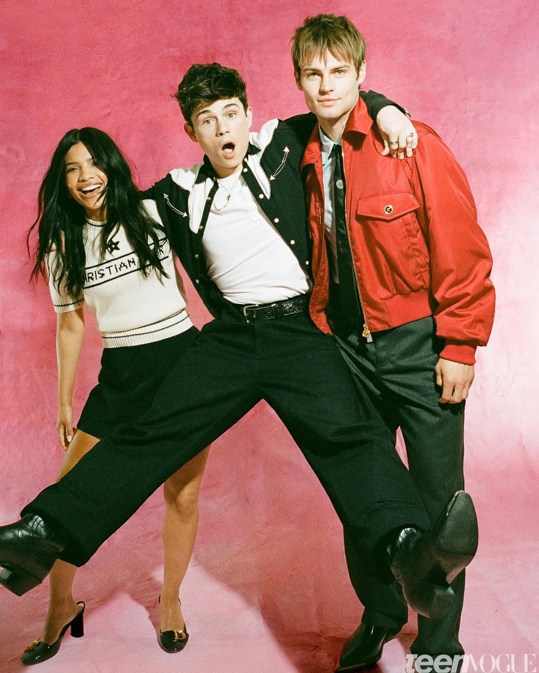 Three young people pose playfully in front of a pink backdrop, channeling the energy of 2026’s hottest YA adaptations—like something straight from BookTok. The woman on the left smiles, while her friends jump and laugh beside her.