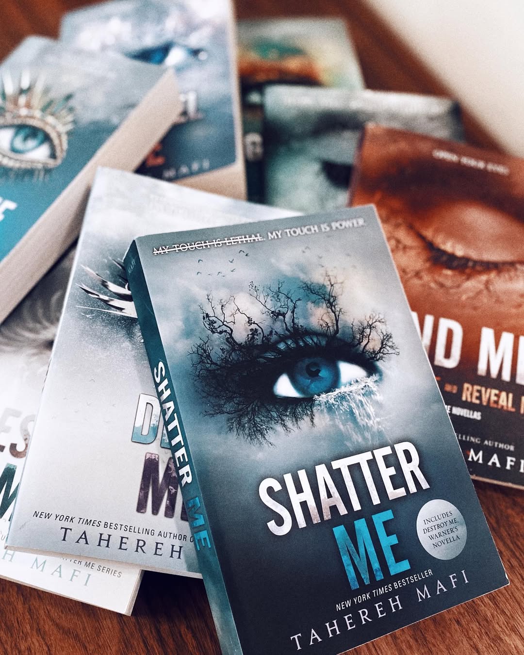 A close-up of several books from the Shatter Me series by Tahereh Mafi spread out on a table, with the iconic blue eye cover—beloved on BookTok—most prominent in the foreground. Perfect for fans of YA adaptations dreaming of a big screen debut.