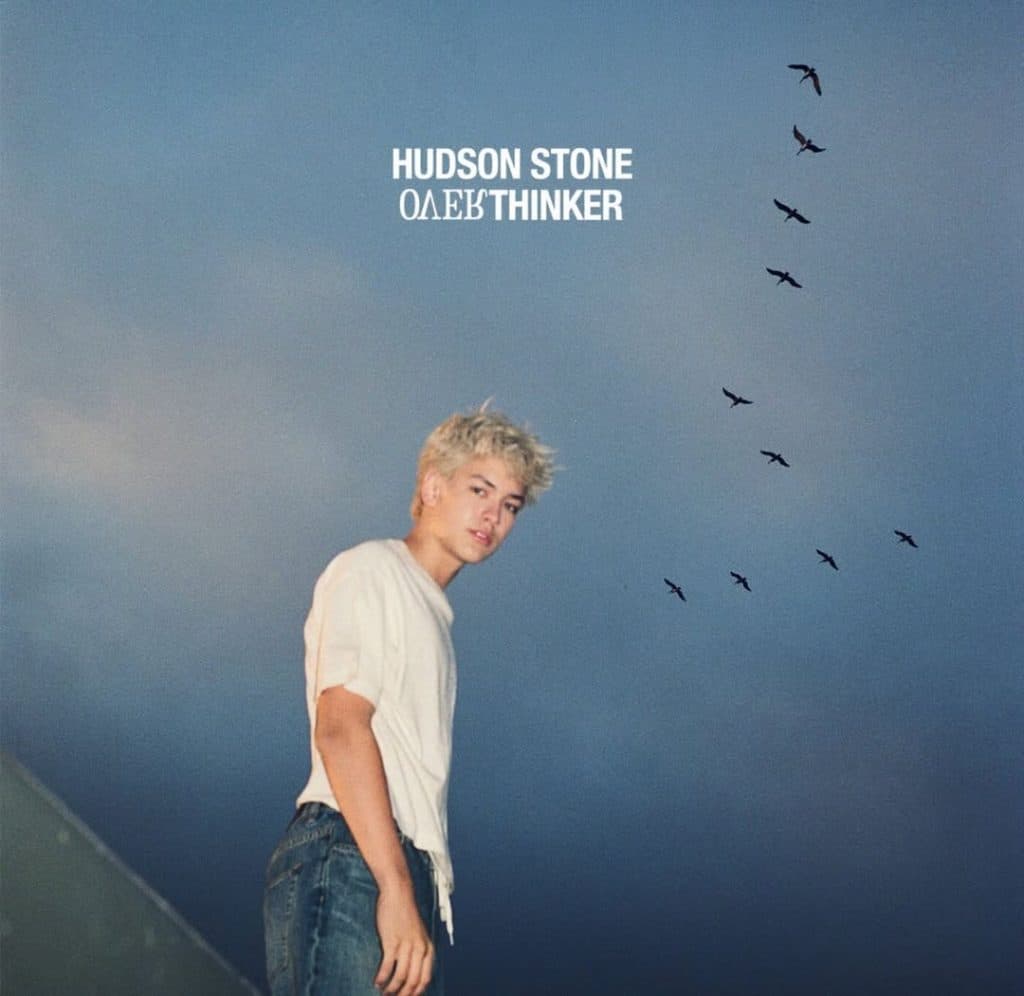 A person with short platinum blond hair stands outdoors under a cloudy sky. Birds fly in a V formation above. At the top, bold text reads "HUDSON STONE" and subtly hints at the thoughtful nature of Hudson Stone, the only thinker.