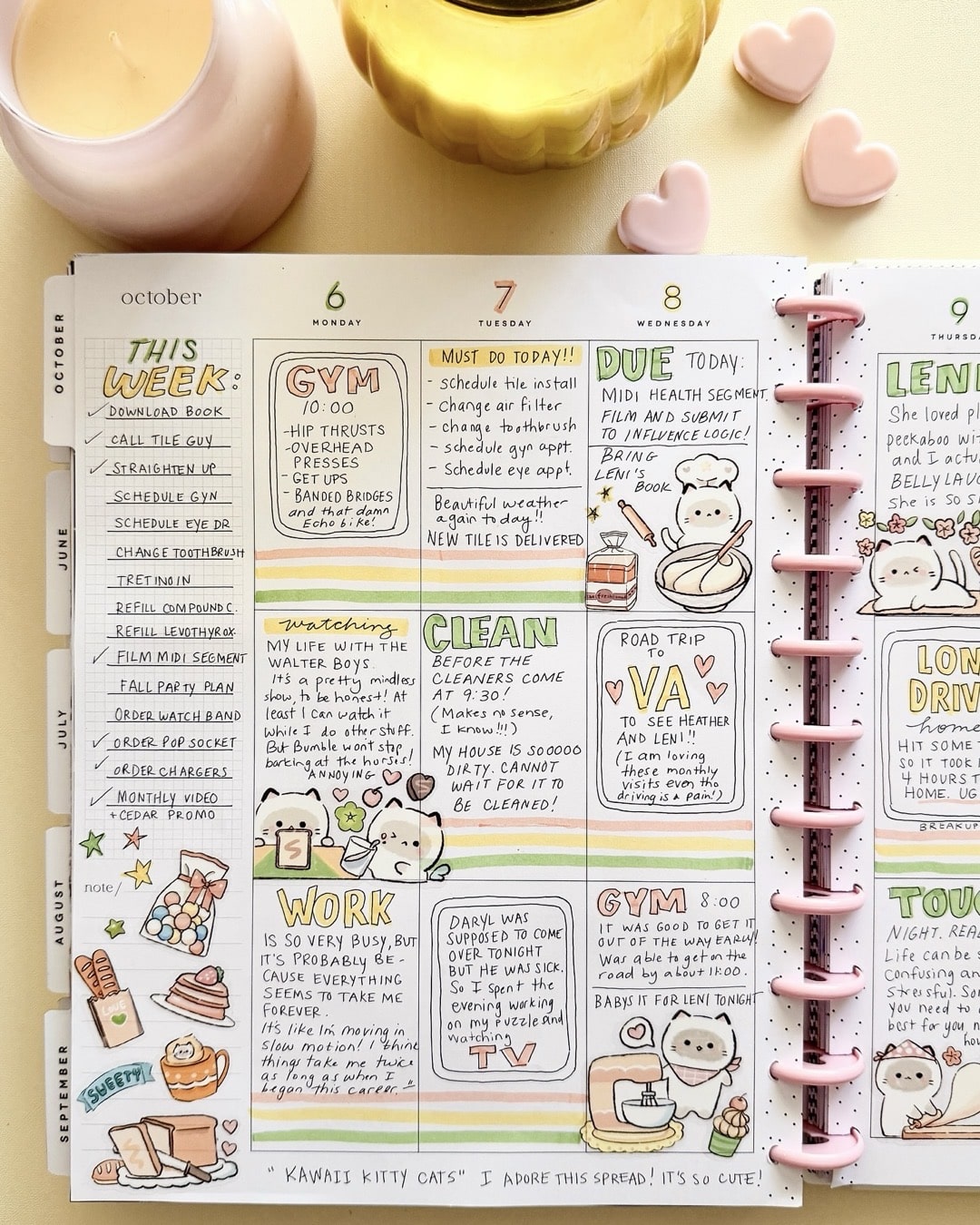 An open planner with colorful handwritten notes, doodles of cats and coffee cups, a pink candle on the left, a yellow vase, and three pink heart-shaped objects on a beige surface—perfect for nixing those back-to-school scaries in style.
