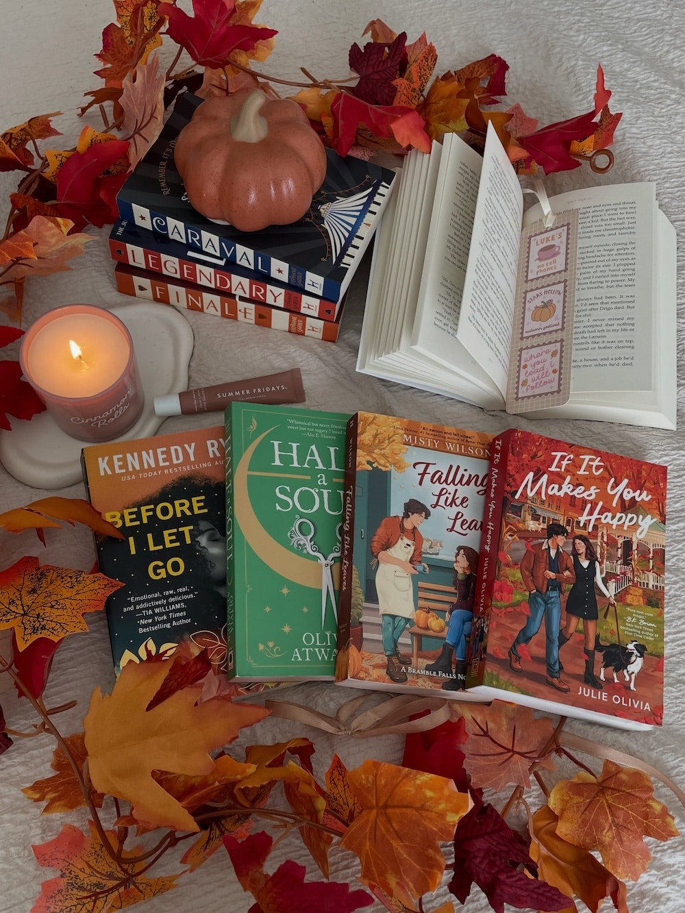 A cozy autumn scene with books, a candle, a small pumpkin, and colorful fall leaves scattered on a blanket. Several open and closed books are displayed, evoking a warm, inviting reading atmosphere perfect for discovering your next Amazing Reads or indulging in the magic of Fall Fantasy.